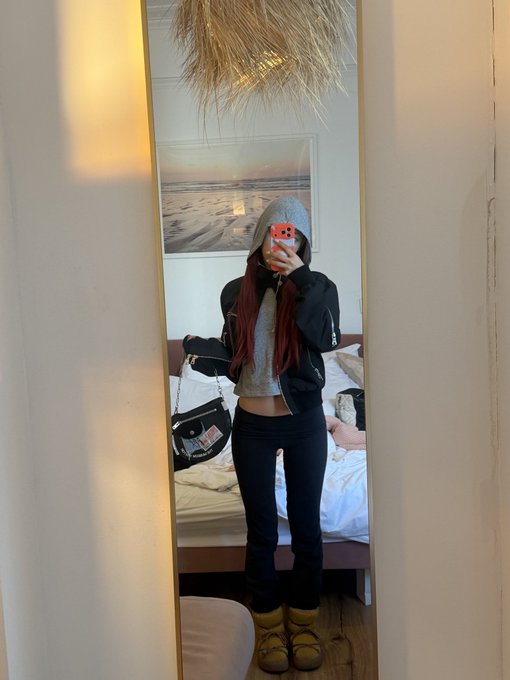 A person taking a mirror selfie wearing a gray hooded top, black jacket, dark pants, and tan UGG-style boots in a bedroom.