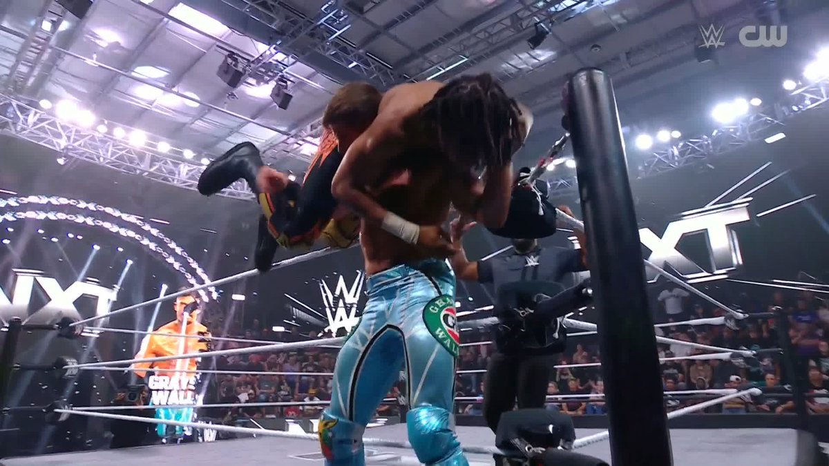 The image shows a WWE NXT wrestling match where a wrestler in turquoise "Grayson Waller" branded tights is executing a high-impact lifting move on an opponent with long dreadlocks, with the "NXT" logo and "CW" network watermark visible in the arena—capturing the brutal moment referenced by the post calling the spot "NASTY."