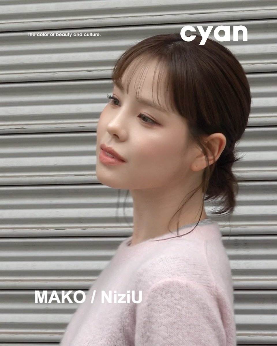 A young woman with dark hair styled in a low bun poses against a corrugated metal background, wearing a pink top, with text reading 'cyan the color of beauty and culture' and 'MAKO / NiziU'.