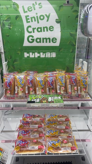 A display in a Japanese store under a green sign reading 'Let's Enjoy Crane Game', showing two shelves of individually wrapped dorayaki (red bean pancake) snacks designed to look like prize machine items.