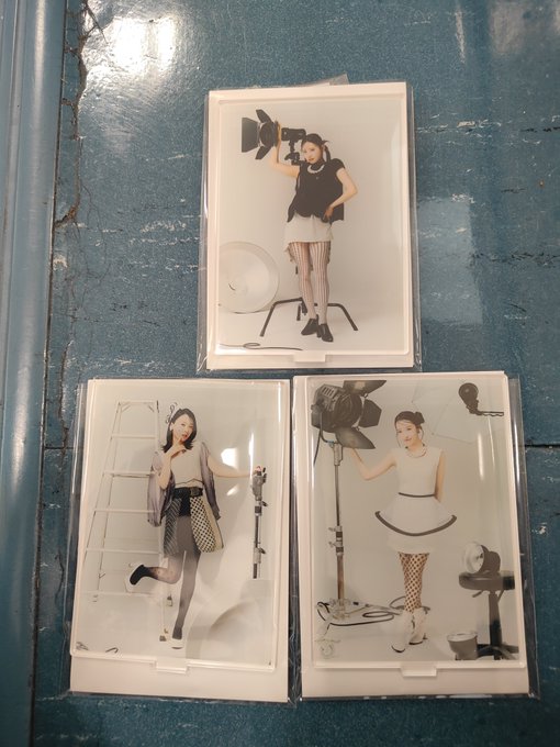 Three packaged white trays or cases featuring black-and-white photos of stylish women posing with photography equipment like a light, ladder, fan, and microphone against a blue surface.