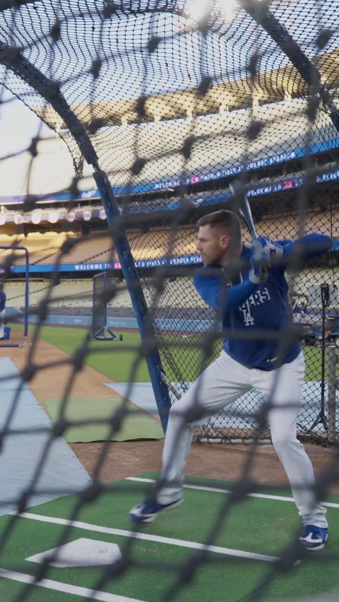 A Los Angeles Dodgers player, wearing jersey number 14, takes batting practice inside the batting cage at Dodger Stadium, viewed through the protective netting, as he prepares for the upcoming October playoff run.