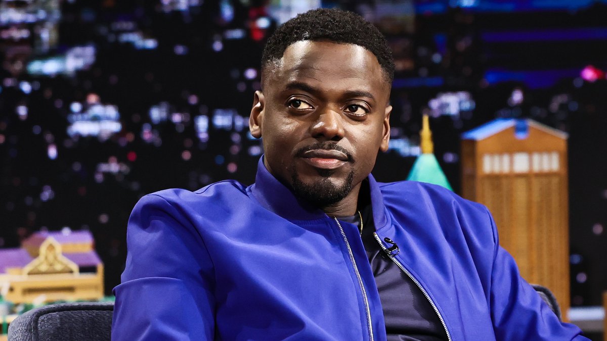 Daniel Kaluuya, wearing a vibrant blue jacket, appears on The Tonight Show with Jimmy Fallon set, smiling subtly during an interview about his role as Spider-Punk in Spider-Verse.