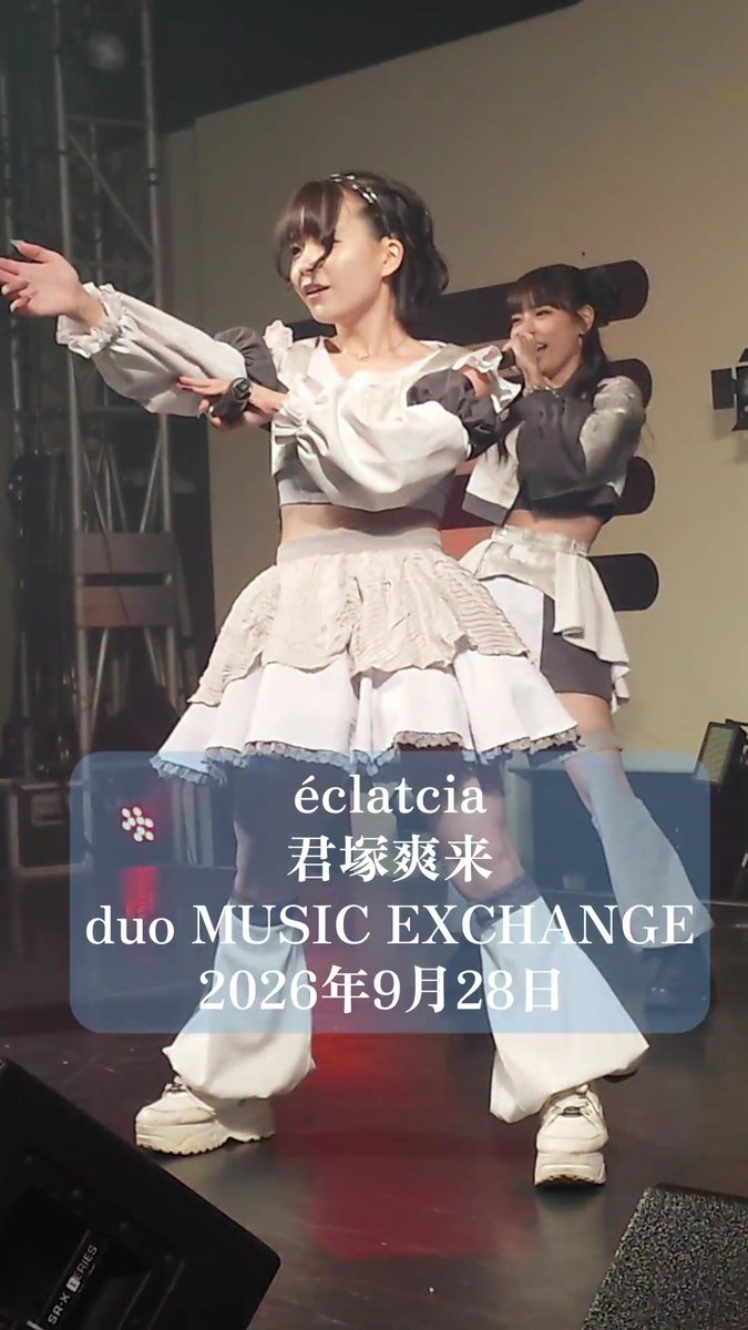 A performance photo of a Japanese idol duo labeled 'éclatcia 君塚爽来 duo MUSIC EXCHANGE 2026年9月28日', featuring two women in coordinated white and gray ruffled outfits dancing on stage.