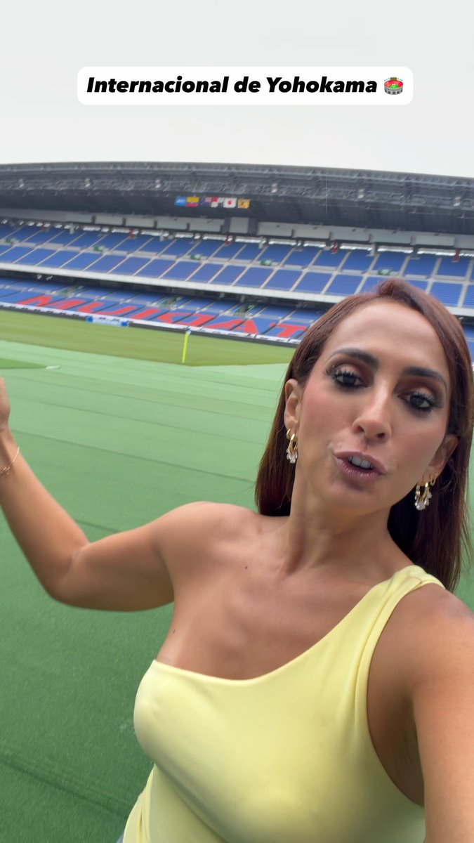 A woman in a yellow top taking a selfie in an empty soccer stadium, with a text overlay reading "Internacional de Yohokama" and a sushi emoji.