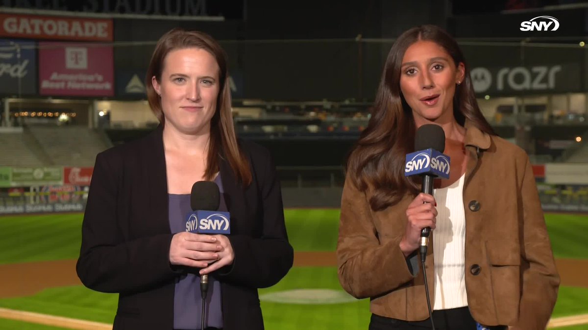Two SNY broadcasters stand on a baseball field at night with SNY-branded microphones, reporting from a stadium featuring visible "Gatorade," "T-Mobile," and "razr" advertisements in the background. The image aligns with the post's description of SportsNite anchors Niki Lattarulo and Chelsea Janes delivering post-game coverage following the Yankees' Wild Card Game 1 victory over the Red Sox.