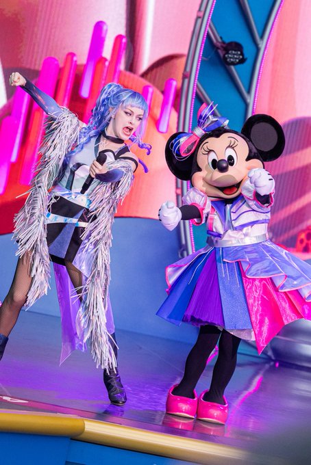Lady Gaga in a striking blue and white fringed outfit performing on stage alongside Minnie Mouse, who is dressed in a coordinating purple and blue gown.