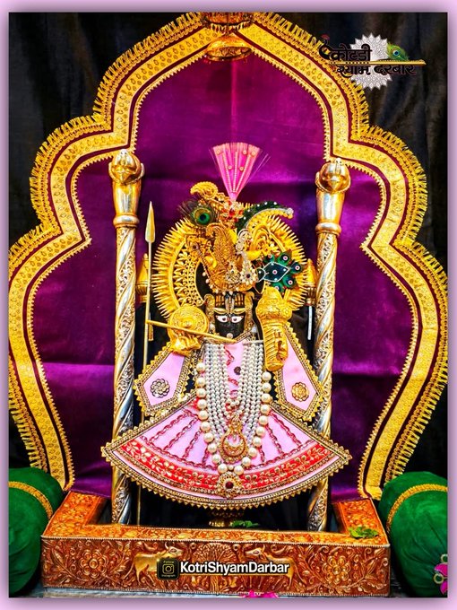 A photograph of an ornately decorated Hindu deity statue, adorned with elaborate golden garments, jewelry, and a crown, seated within a decorative archway, watermarked 'KotriShyamDarbar.'