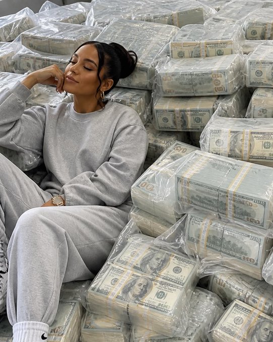 A woman in a gray sweatsuit lying peacefully amid numerous plastic-wrapped stacks of US currency.