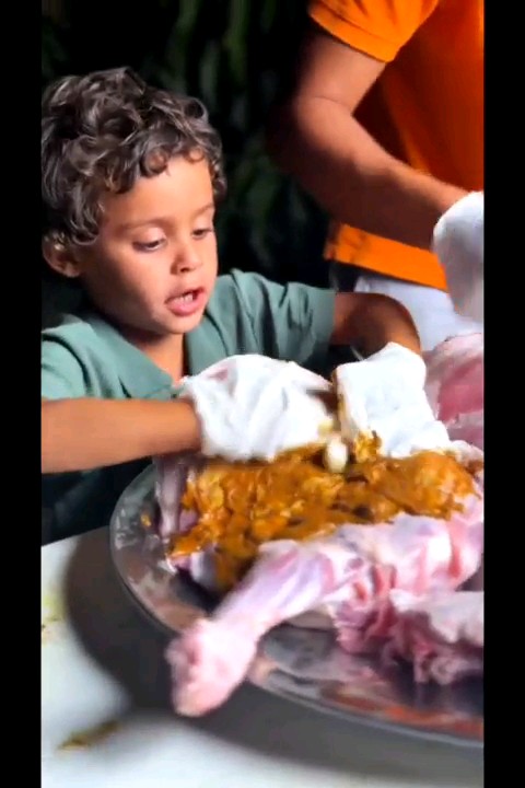 A young boy with curly hair looks with interest at a large turkey covered in gravy and marshmallows on a platter.