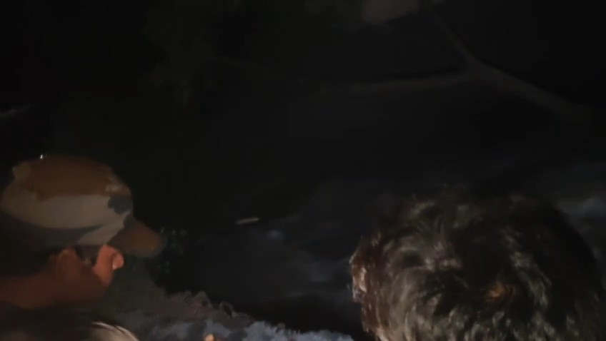 A dark, low-quality image showing the back of a person's curly-haired head and a hand holding a piece of bread or food in a dimly lit setting.