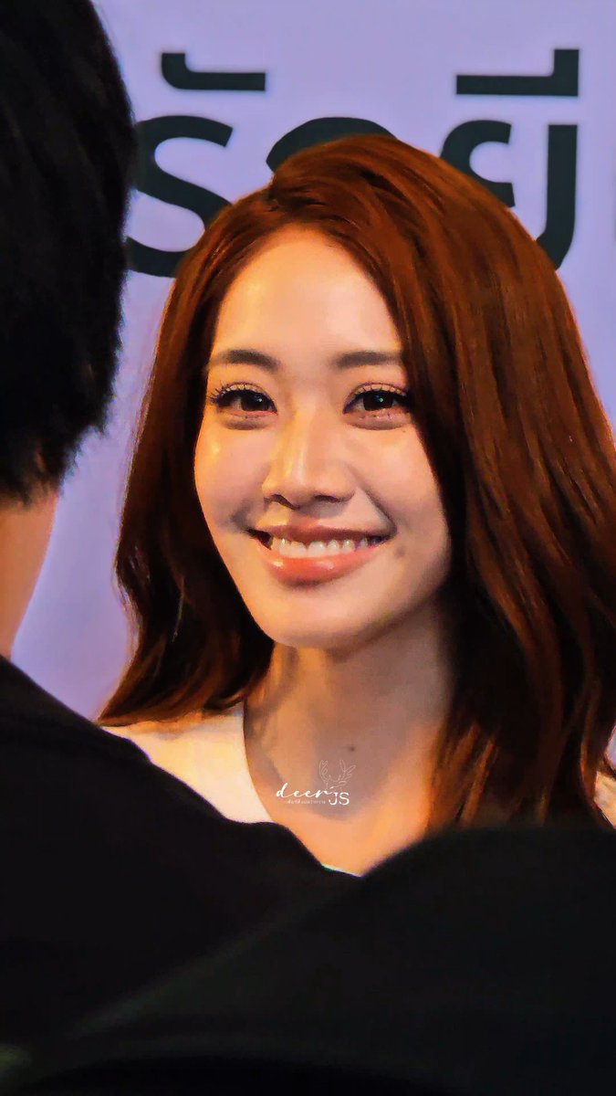 A close-up portrait of a smiling Asian woman with long auburn hair, with a watermark 'dear JS' visible at the bottom and partial Korean text in the background.