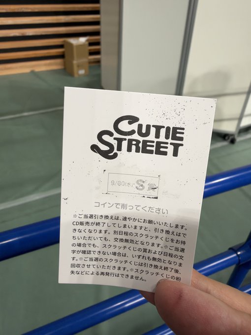 A hand holding a small printed card with the text 'CUTIE STREET' and a QR code section, containing Japanese instructions asking the user to scan it with their smartphone.