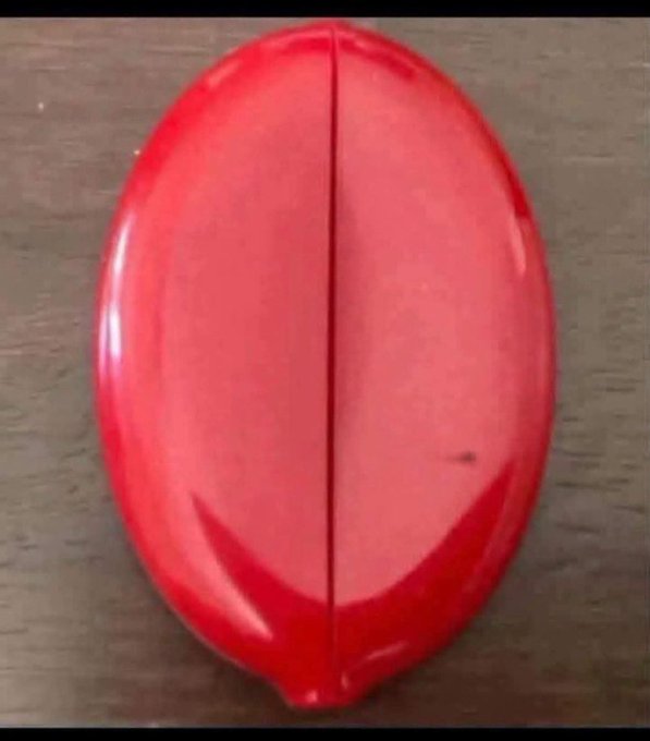 A glossy red oval object with a central seam rests on a wooden surface.