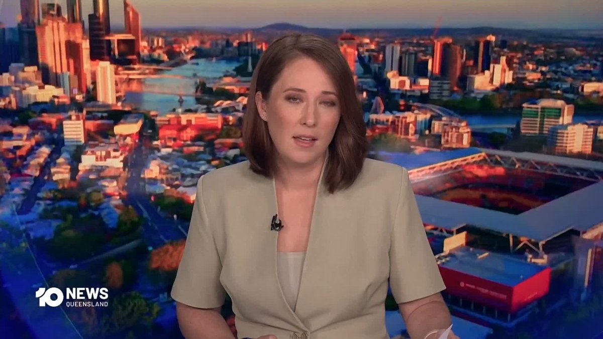 A female news anchor with shoulder-length brown hair, wearing a tan top, presents the news on 10 News Queensland with a cityscape backdrop.