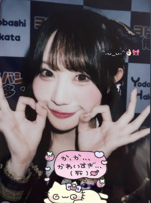 A selfie-style photo of a young woman with dark hair and bangs posing with her hands near her face, with decorative stickers including a cat, strawberries, and a speech bubble containing Japanese text 'か、か…かわいいすぎ…(死)' and the handle '^..^'.