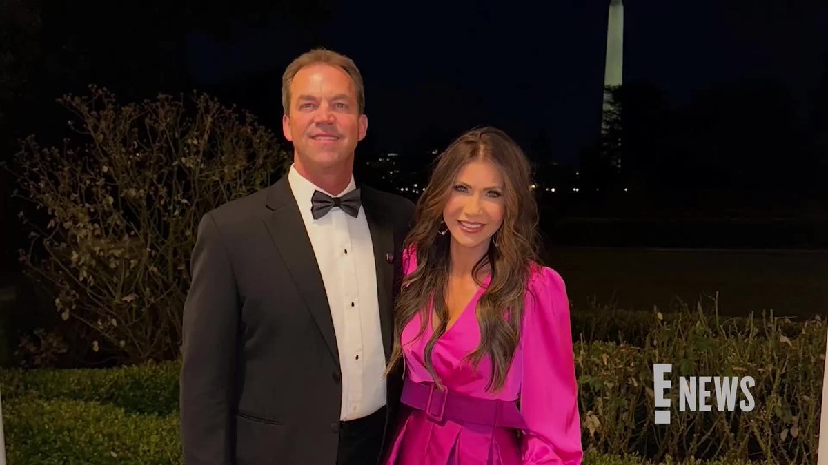 A man in a black tuxedo and a woman in a bright pink dress pose together at night with the Washington Monument visible in the background; the image has an E! NEWS watermark.