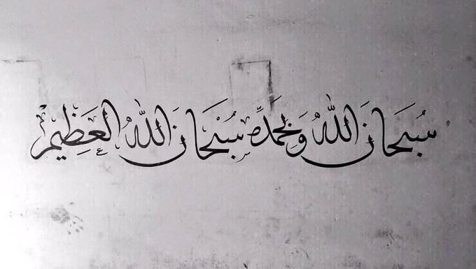 Black Arabic calligraphy painted on a white surface, displaying the Islamic phrase 'Bismillah ir-Rahman ir-Rahim' (In the name of Allah, the Most Gracious, the Most Merciful).