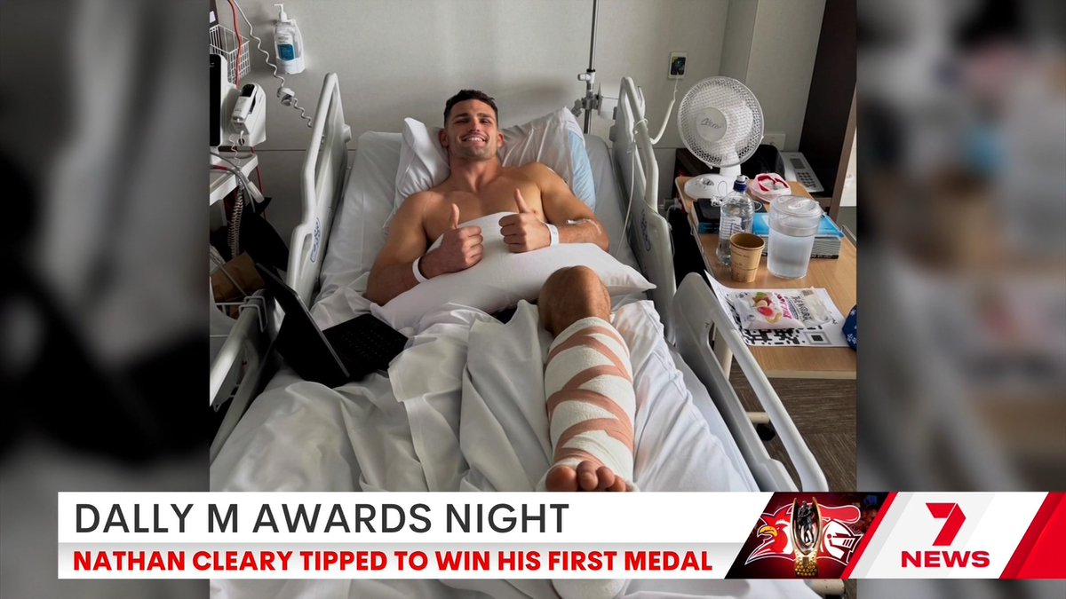 Nathan Cleary gives a double thumbs-up from his hospital bed, smiling with his right leg heavily bandaged following hip surgery, as the 7 News graphic announces "DALLY M AWARDS NIGHT - NATHAN CLEARY TIPPED TO WIN HIS FIRST MEDAL." The image illustrates his absence from the ceremony, which he is expected to win despite recovering from the injury.