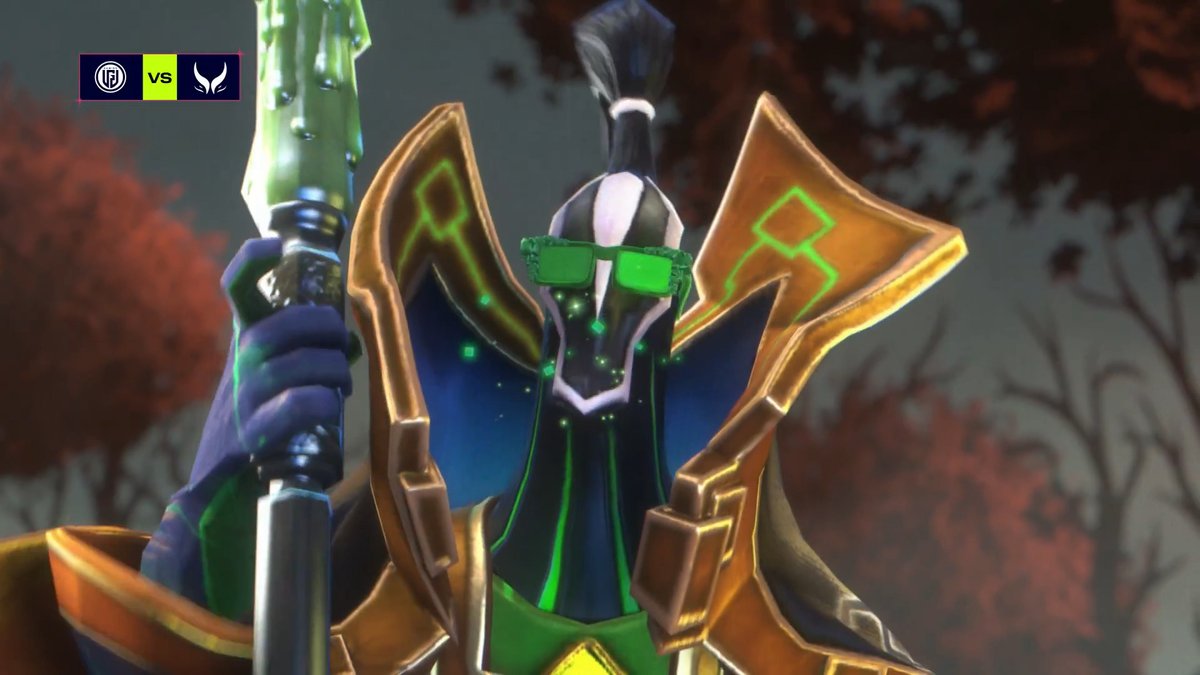 A 3D-rendered character wearing green glasses and ornate gold shoulder armor, holding a staff, with 'TS vs TUN' logos in the upper left corner.