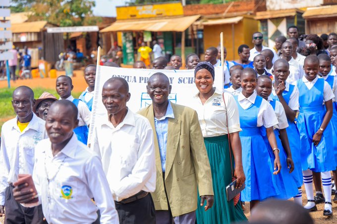 Group photo of students and adults, including teachers and community members in front of a banner reading "NYAGWA PRIMARY SCHOOL," with students wearing blue and white uniforms.