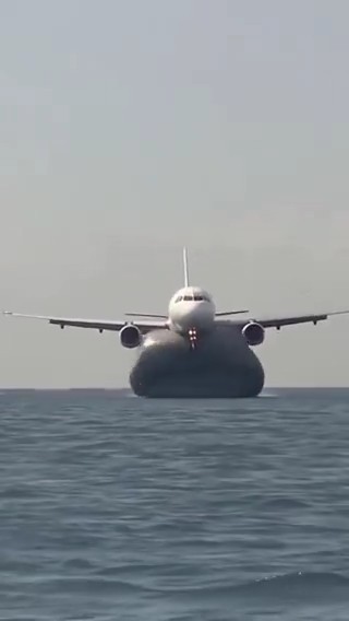 A commercial airplane flies low over the ocean, heading directly toward the camera with its landing gear extended.