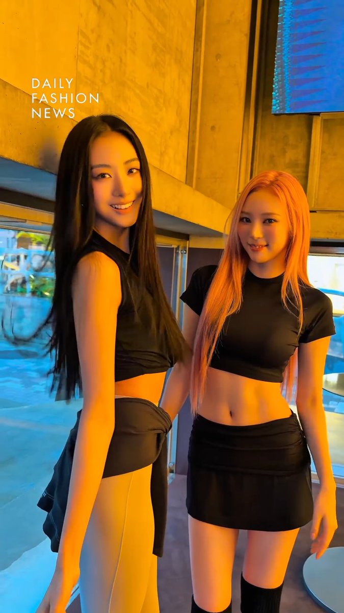 Two young women posing together in black crop tops and skirts; the image has 'DAILY FASHION NEWS' text overlaid.