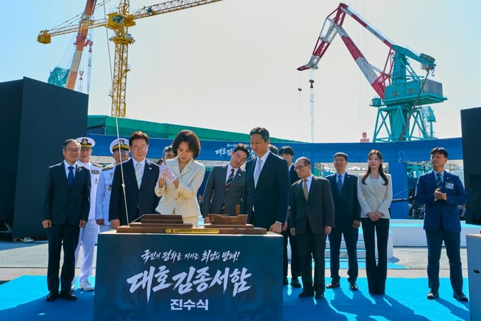 A groundbreaking ceremony for "대호건설중공업" (Daeho Construction & Engineering) with Korean text "우리 행복을 지는 사람 많은 이야기 옆에" and "건축종식" (translation, attended), featuring officials in suits and naval uniforms with cranes in the background.