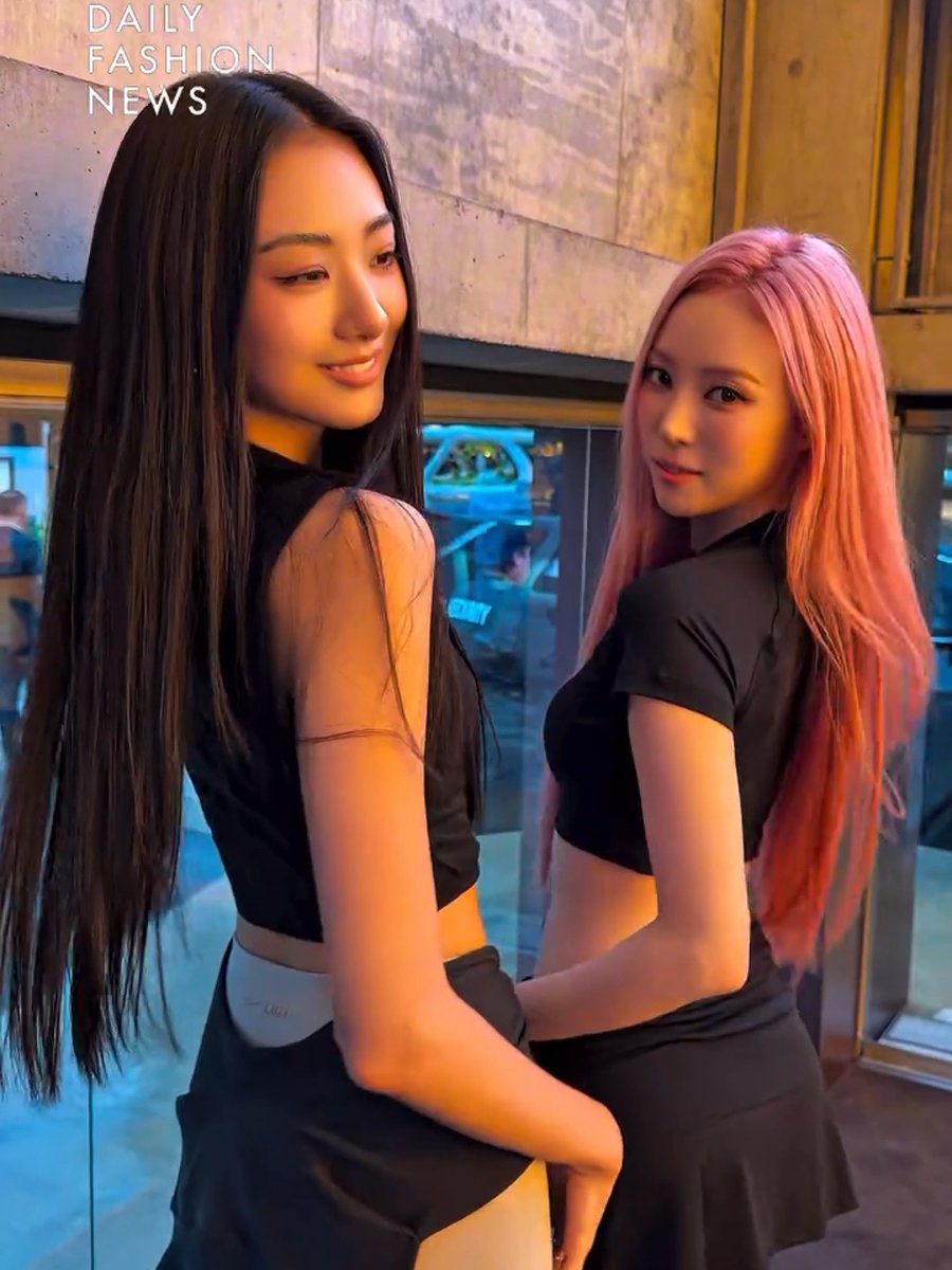 Two young women posing together at night, one with long dark hair and the other with pink hair, both wearing black crop tops, with text reading 'DAILY FASHION NEWS' in the top left.