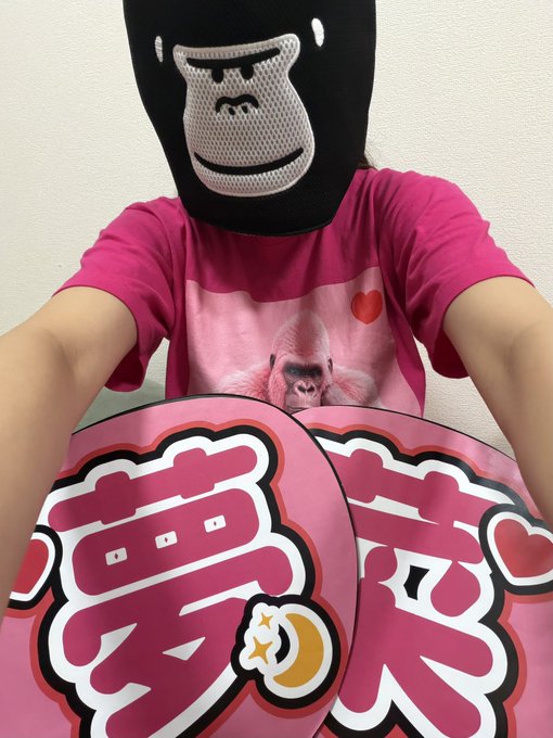A person wearing a gorilla mask and a pink t-shirt featuring a gorilla graphic and a heart holds two pink signs with bold Japanese characters (募 and 炎) and a crescent moon/flower design, appearing as a fan eagerly awaiting Yunatama (a Japanese comedian duo known for their gorilla-themed personas). The playful gorilla imagery and Japanese fan-sign lettering directly reflect anticipation for the comedy act.