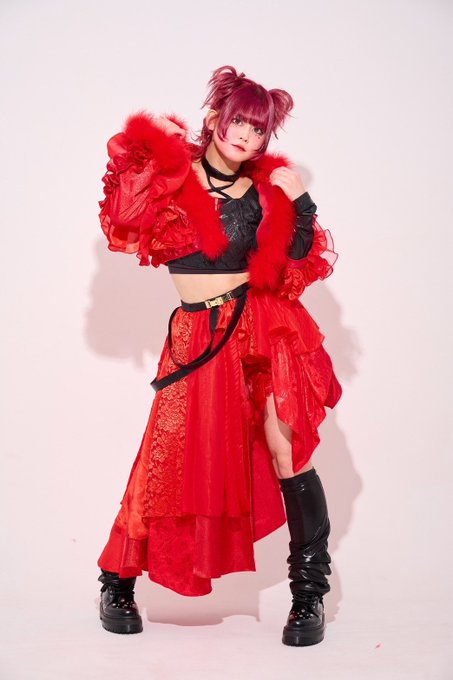 A young woman with pink hair poses confidently in a striking red ensemble featuring a fur-trimmed jacket, layered skirt, and black platform boots. The image accompanies an announcement about AIBECK member Hinata Yuka's graduation due to a worsening chronic illness, with her farewell performance scheduled at CLUB CITTA' on her birthday.