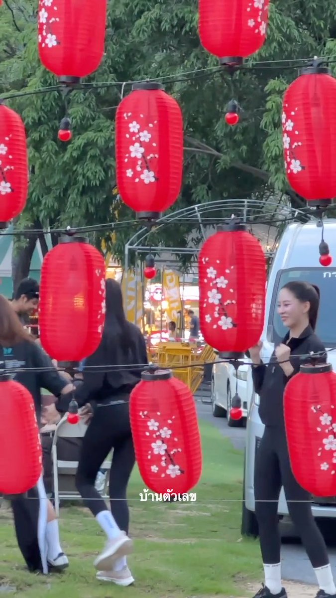 People in black outfits stand among hanging red Japanese-style lanterns with cherry blossom designs, with Thai text "บ้านตัวเลข" overlaid.