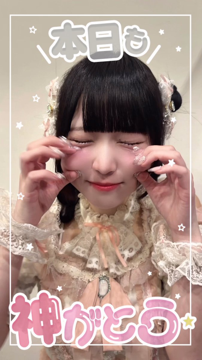 A young woman with dark hair and bangs, wearing a frilly pink dress, smiles with her eyes closed while touching her cheeks, framed by Japanese text that reads "本日も" and "神がどる".
