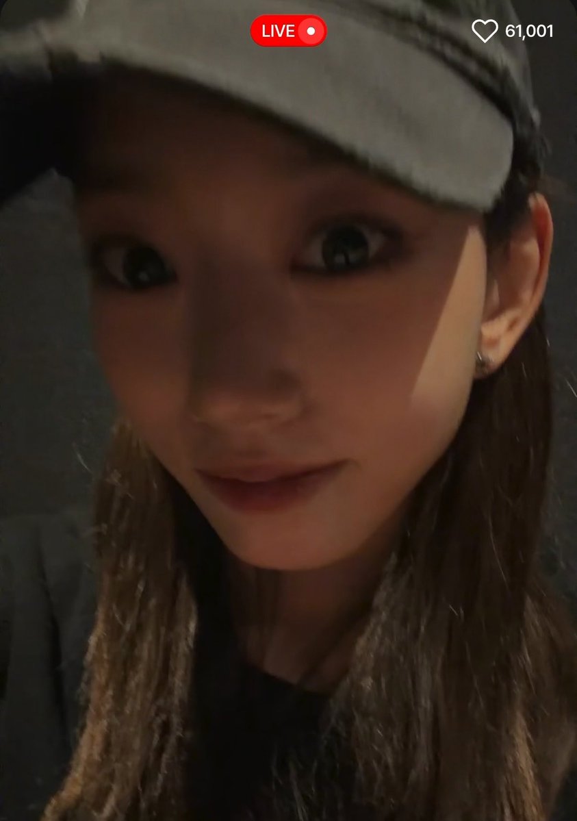 A close-up live selfie of a person wearing a gray cap, showing a 'LIVE' indicator and '61,001' likes on the screen.