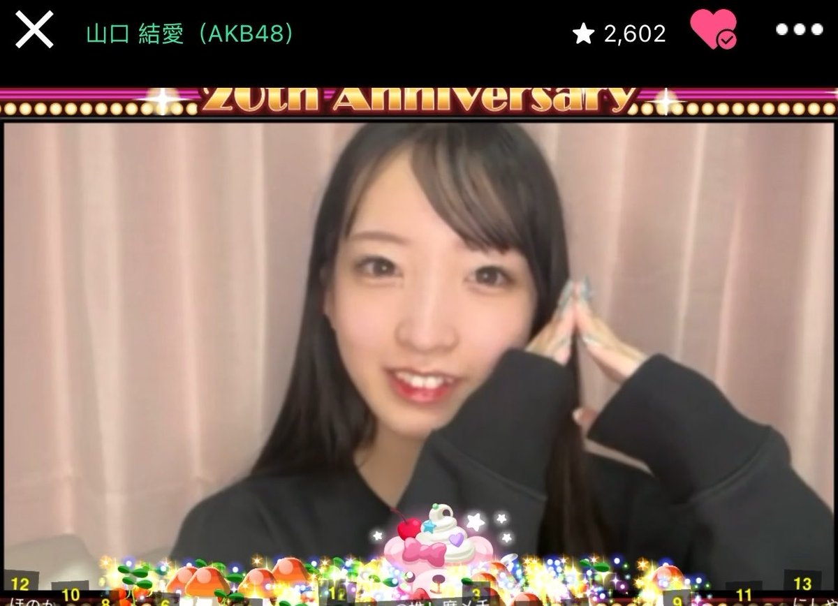 A livestream screenshot of AKB48 member 山口 結愛 (Yamaguchi Yua) celebrating the 20th Anniversary, with 2,602 likes displayed, the streamer making a hand gesture near her face with anniversary-themed graphics including a cake and presents.