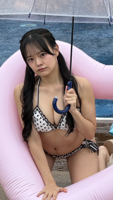 A young woman in a black and white polka dot bikini holds a clear umbrella while sitting on a pink inflatable float.