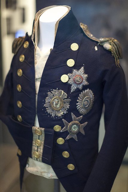 archeohistories's tweet photo. The historical uniform coat worn by British Admiral Horatio Nelson at the Battle of Trafalgar in 1805. The coat is on display at the National Maritime Museum in Greenwich, London... 

The coat with the hole in the left shoulder caused by the musket ball that killed him. The musket shot struck Nelson down through his left shoulder, smashed two ribs, and tore through his left lung, severing a major artery on the way.

(Battle of Trafalgar – a 1805 naval battle during the Napoleonic Wars in which Admiral Nelson’s fleet defeated the French and Spanish navies, securing British naval supremacy and preventing Napoleon’s planned invasion of Britain)... 

This naval coat belonged to Admiral Horatio Nelson, one of Britain’s greatest military heroes, who was fatally wounded during the Battle of Trafalgar on October 21, 1805. The engagement, fought off the coast of Spain, pitted the British Royal Navy against the combined fleets of France and Spain during the Napoleonic Wars. Nelson’s leadership and tactical brilliance secured a decisive British victory that ensured Britain’s naval dominance for the next century, but it cost him his life.

As Nelson stood on the deck of HMS Victory, he was struck by a musket ball fired from the French ship Redoutable. The bullet entered his shoulder and lodged in his spine, leaving him paralyzed. He was carried below deck, where he lived long enough to learn that the British had won the battle. His final reported words, “Thank God I have done my duty,” became part of naval legend.

The coat, now preserved at the National Maritime Museum in Greenwich, still bears the tear left by the fatal shot, along with traces of blood. It stands as a haunting relic of both heroism and mortality, symbolizing the price of victory and the personal cost of empire.

Nelson had previously lost his right arm and the sight in one eye in earlier battles, yet continued to command at sea, earning near-mythic status in Britain as the embodiment of courage and sacrifice.

#archaeohistories