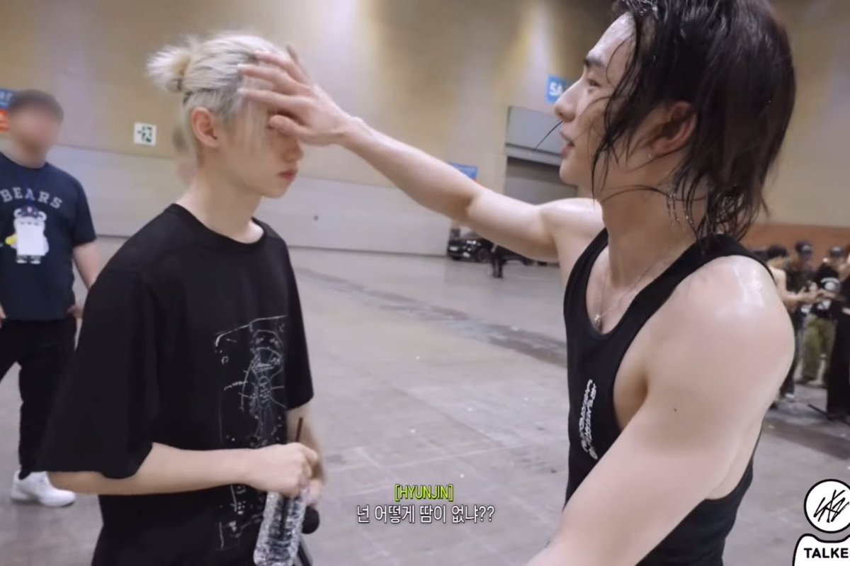 Two people in black shirts interact in what appears to be an indoor venue, with one person touching the other's forehead; Korean subtitles read '[HYUNJIN] 넌 어떻게 닮이 없냐??' with a 'TALKER' logo.