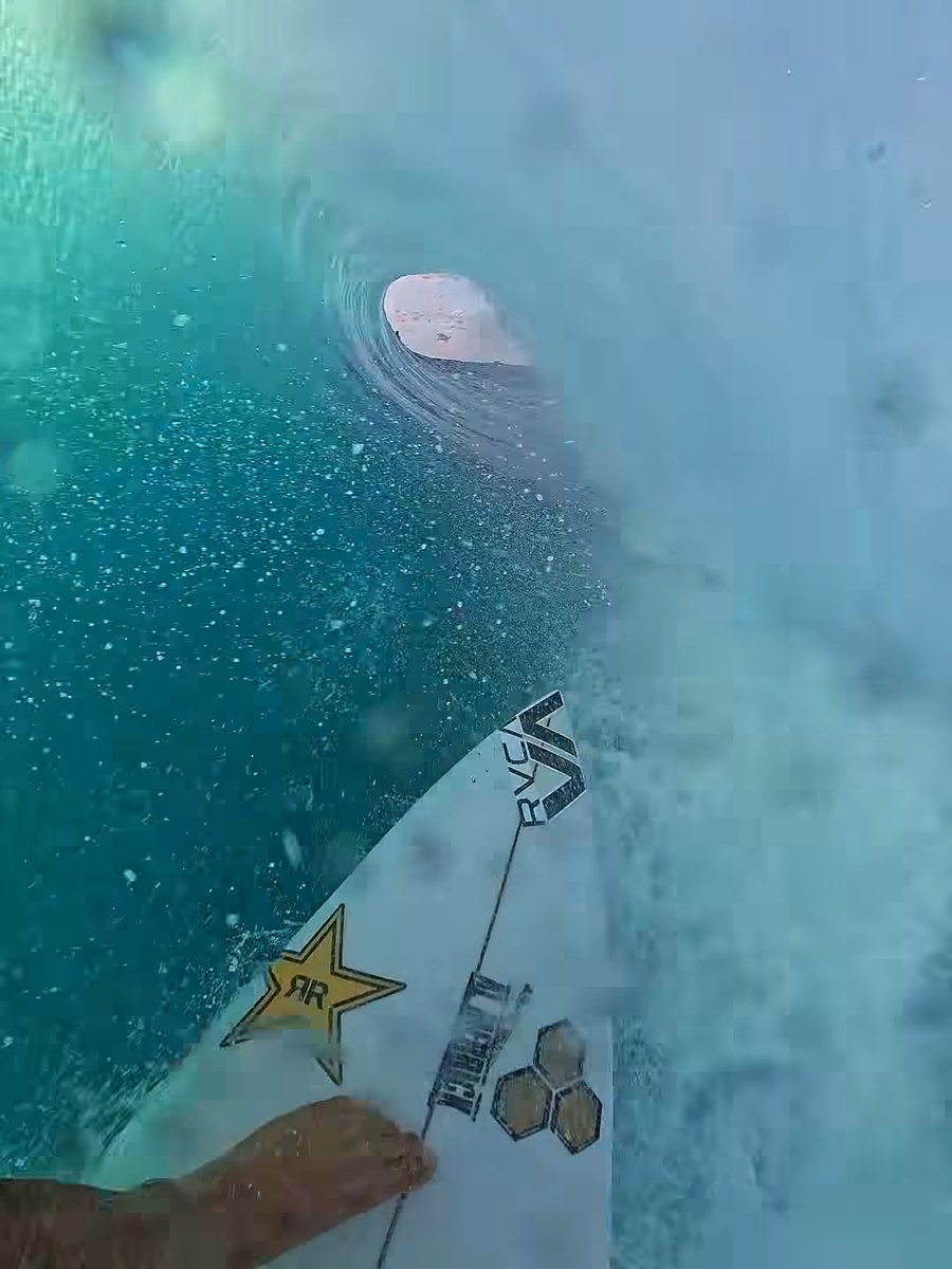 A first-person view of a surfboard or paddleboard with "RVCA" and "ROCKSTAR" stickers floating on water.