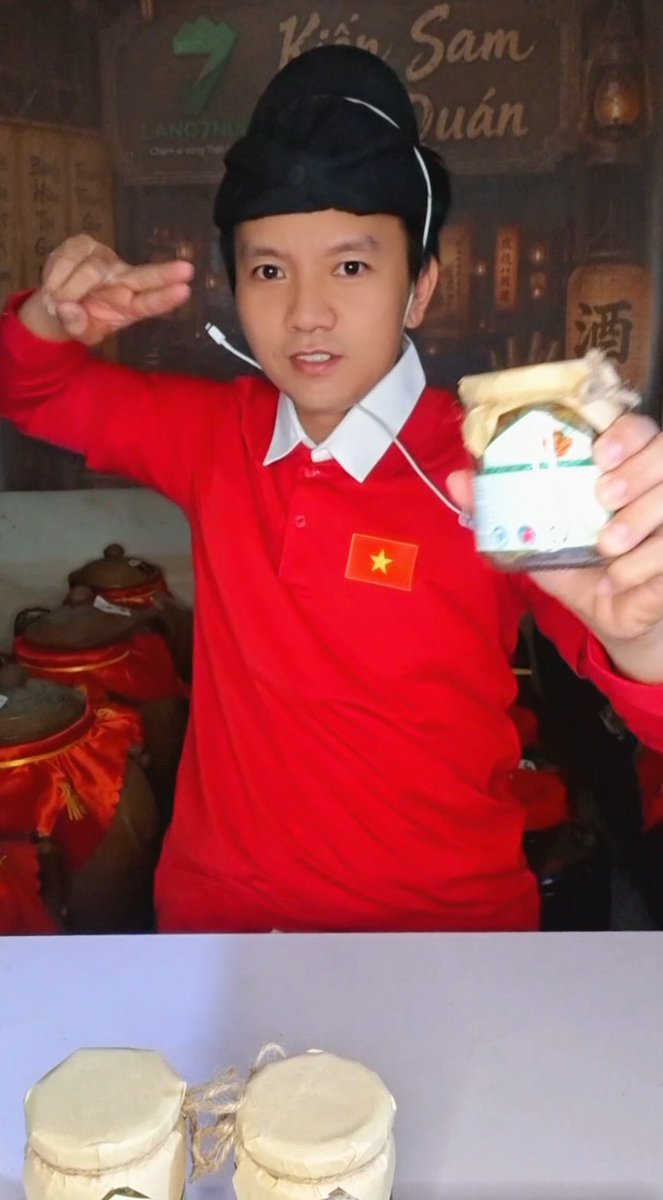 A man wearing a red polo shirt with the Vietnamese flag and a black traditional hat holds up a jar labeled "Kiếm Sâm Quán" while making a salute gesture, evoking a playful Detective Bao aesthetic as referenced in the caption about Zhan Zhao. Behind him are more jars, and a second image below shows two additional cloth-wrapped jars.