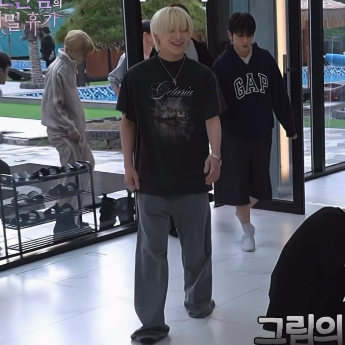 A screenshot from a Korean variety show features a smiling young man with blonde hair wearing a black 'Ciclama' graphic t-shirt and grey jeans, with the text '그린의' visible in the bottom right corner.