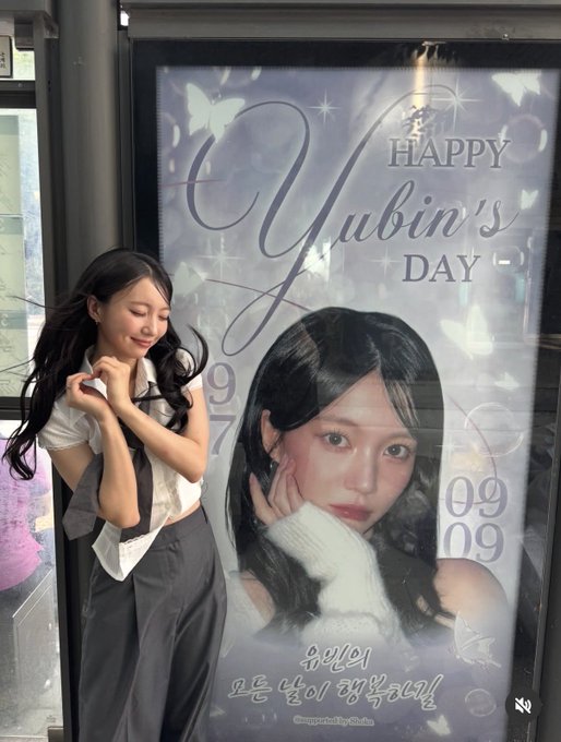 A woman poses next to a poster that reads 'HAPPY Yubin's DAY' with a photo of her, butterflies, and Korean text celebrating her birthday.