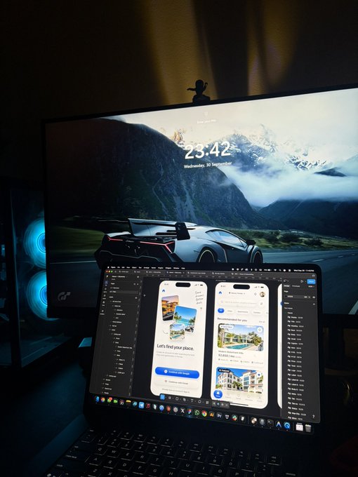 A desk setup with a laptop showing a web design next to a monitor displaying a car wallpaper and the time '23:42 Wednesday, 30 September'.