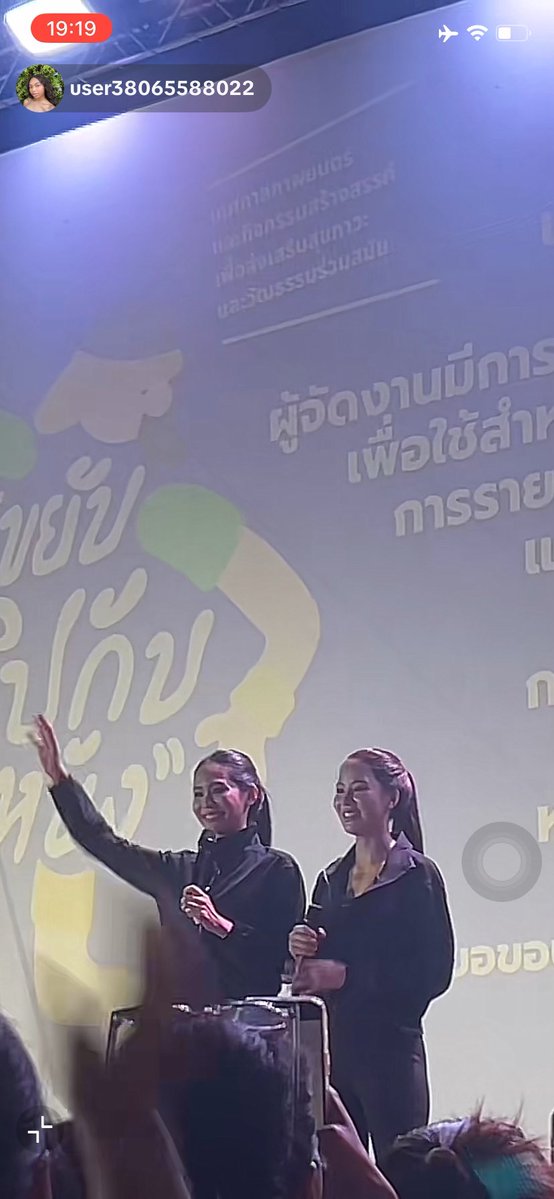 A screenshot showing two women in dark blazers waving from a stage with Thai text on the backdrop and the username 'user38065588022' at the top.