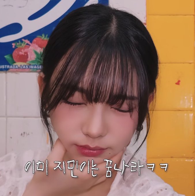 A young woman with dark hair and bangs closes her eyes while touching her cheek, with Korean subtitles at the bottom of the image.