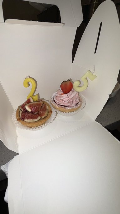 Two tarts decorated with candles shaped like "2" and "5," likely celebrating a 25th birthday, sit in a white bakery box. The image's caption about spotting someone (Yeongjae) being filmed by a crowd suggests the celebratory moment captured an unexpected celebrity encounter during what was meant to be a casual TikTok filming session.