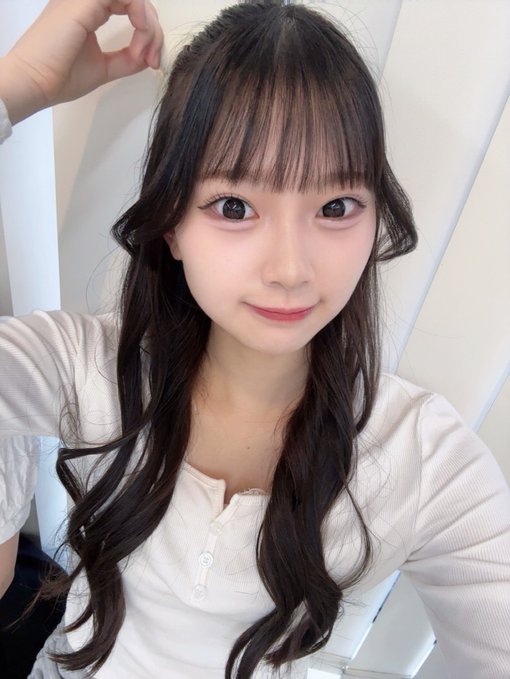 A young woman with long wavy dark hair and bangs smiles softly in a selfie, wearing a white top and touching her hair near her face, with the hashtag #佐藤朱緋 indicating this is Sato Shuki. The caption mentions a ribbon that's barely visible in her hair, matching the subtle hair accessory in the photo as she wishes followers a good night.