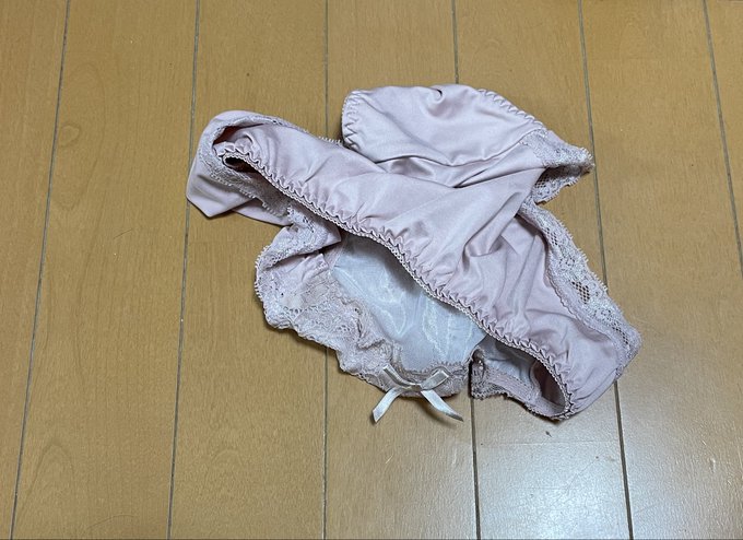 A pair of light pink satin and lace-trimmed women's underwear lies crumpled on a wooden floor.