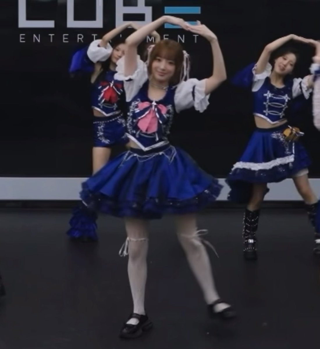 Three female performers dance on stage in matching blue and white frilly outfits, with an 'ENTERTAINMENT' sign visible in the background.