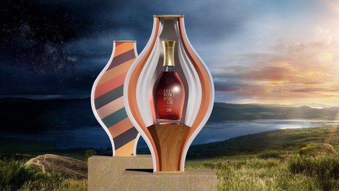 A bottle of Glenfarclas 50 Year Old whisky displayed in a decorative wooden and striped case, set against a dramatic landscape with a starry night sky transitioning into a sunset.